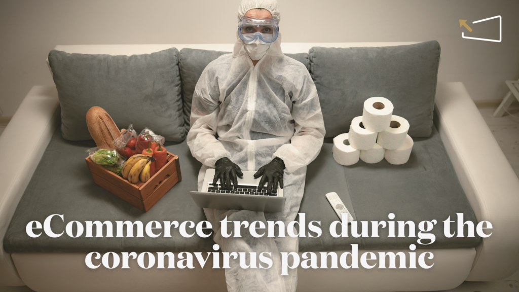 Person in a PPE suit shops online on a couch with groceries and toilet paper.